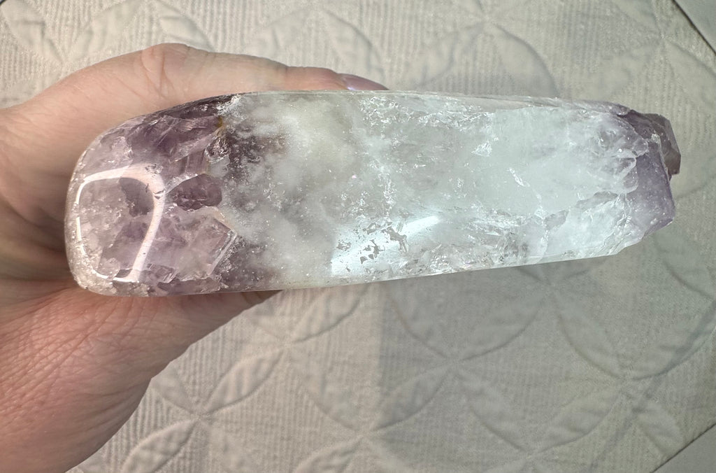 Hand holding a crystal with a white and purple color pattern on a textured surface