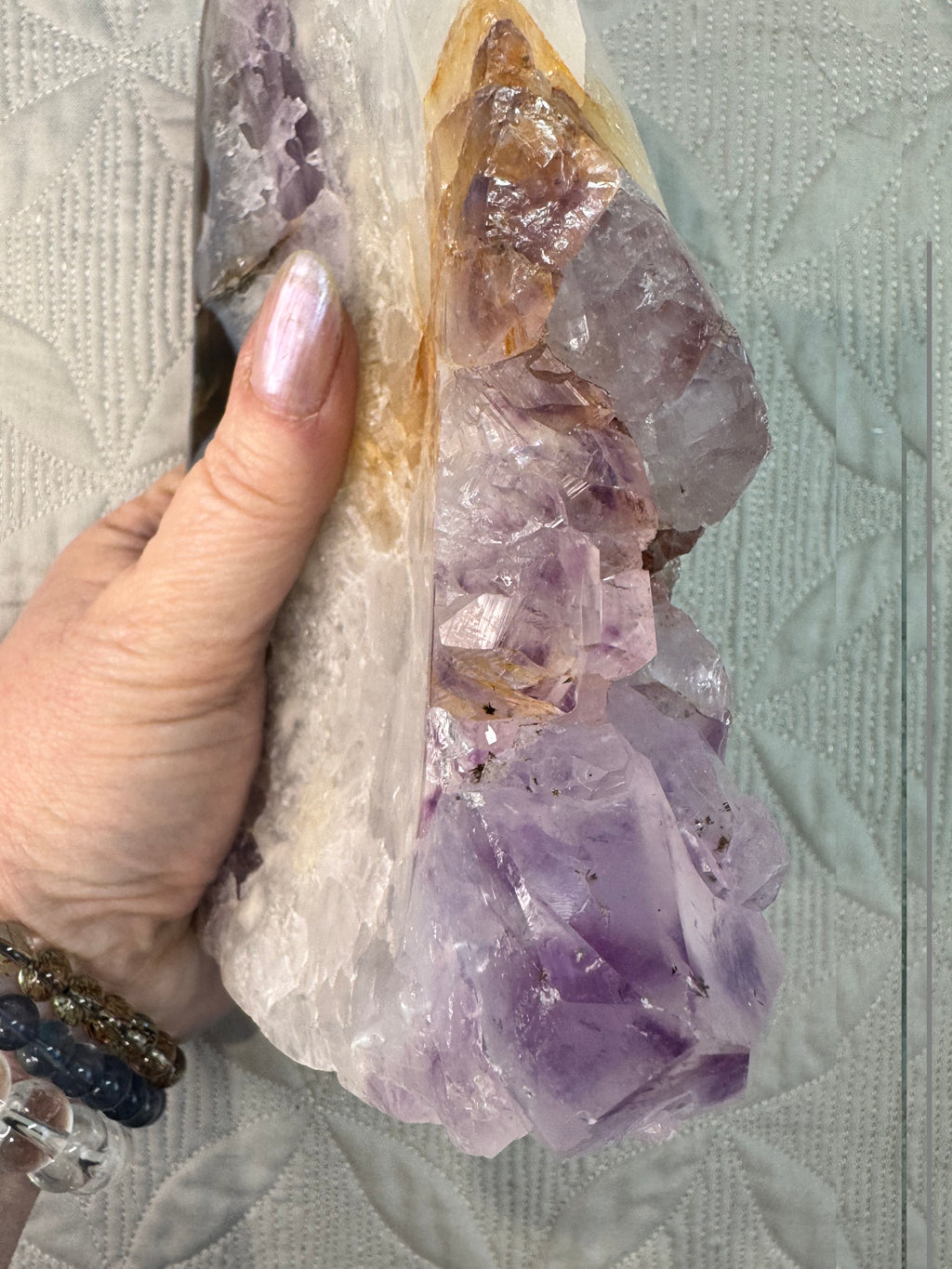 Amethyst crystal cluster held by a hand on a textured surface