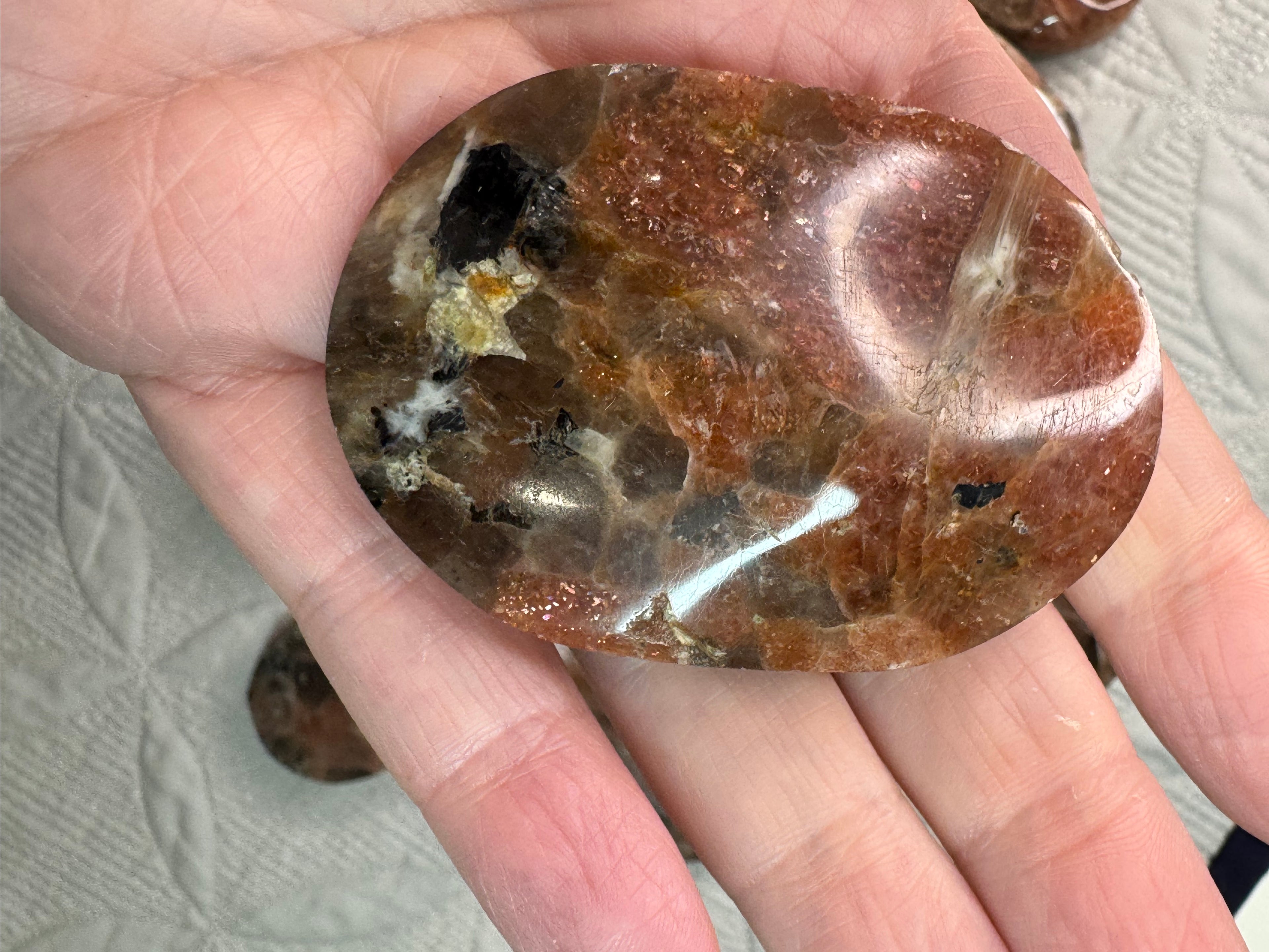 Hand holding a polished brown stone with visible veins on a textured surface