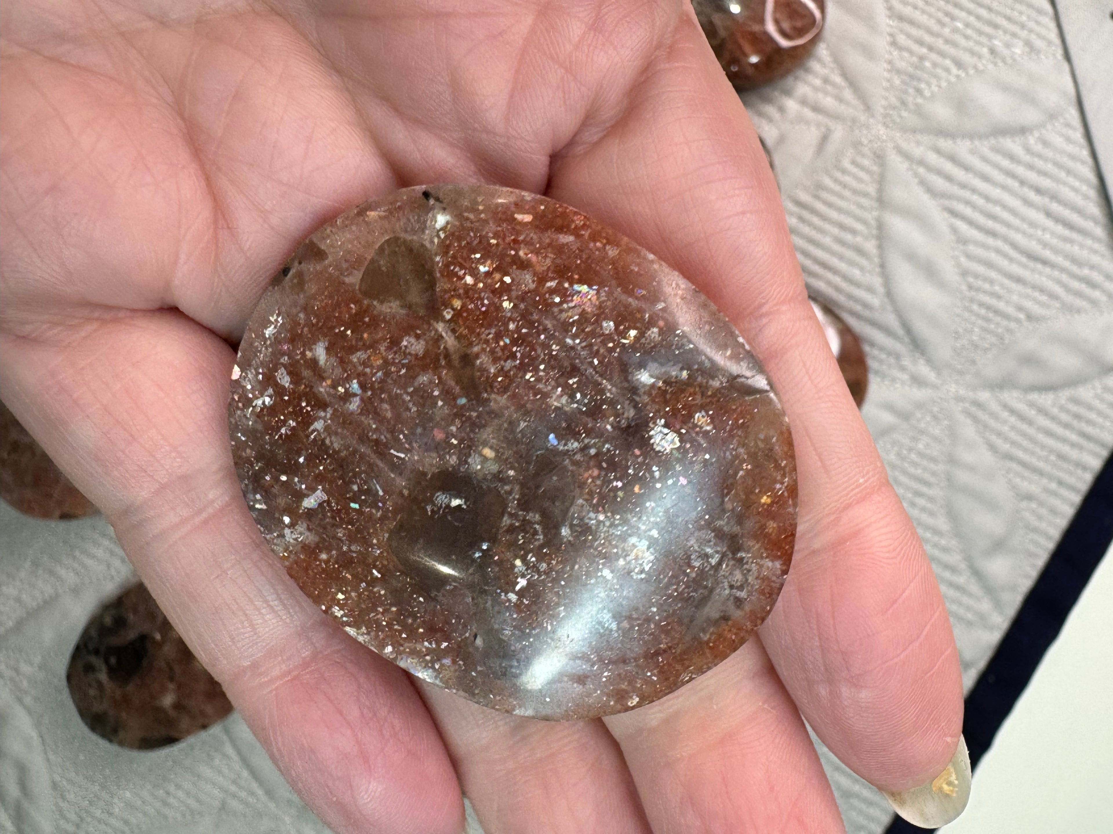 Hand holding a clear crystal with brownish tint on a light background