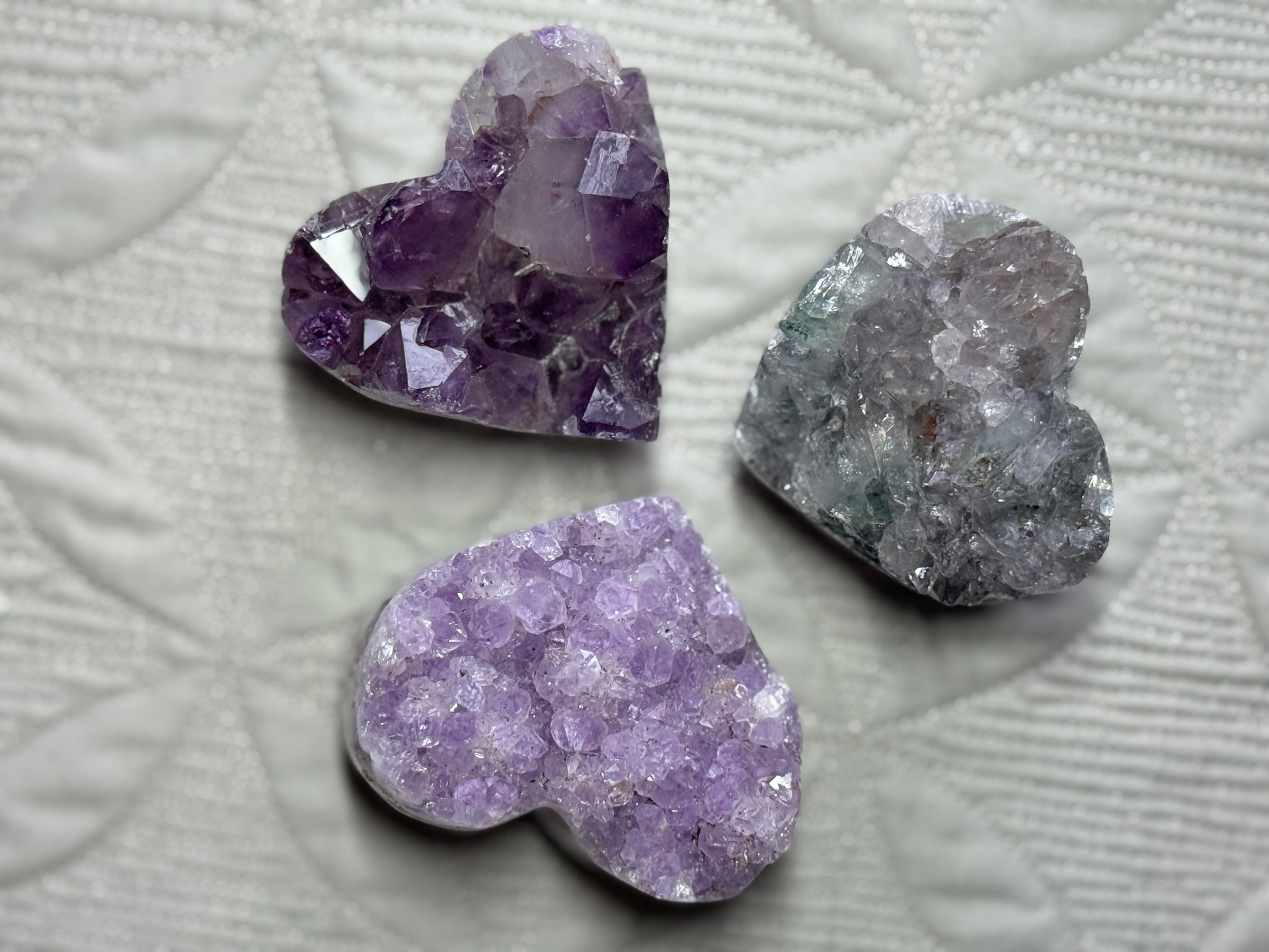 Three purple crystal heart shapes on a textured light gray background