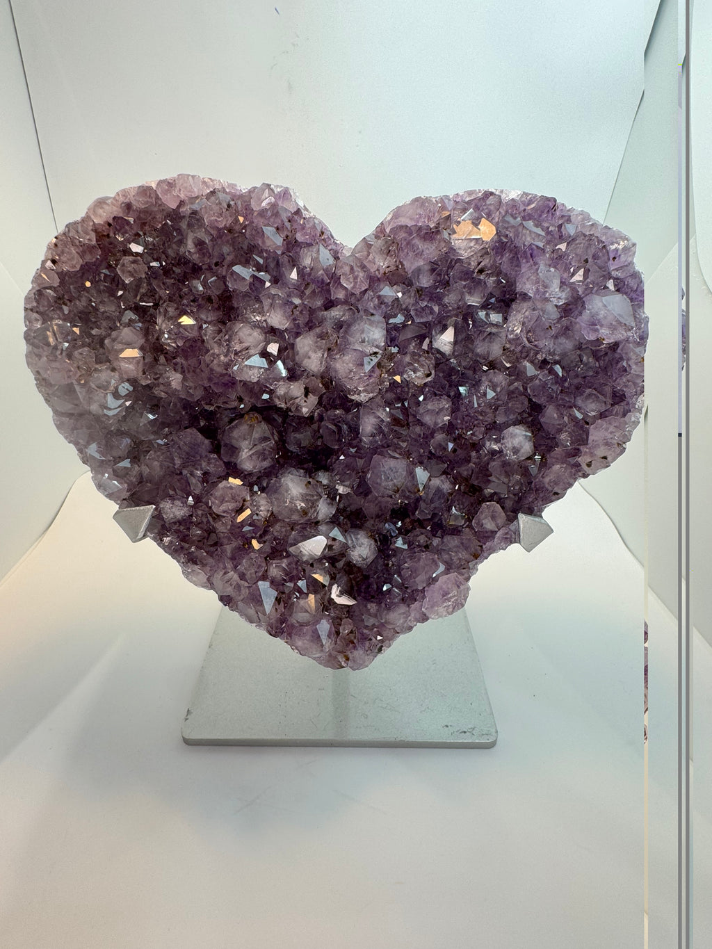 Purple amethyst heart crystal in silver stand, neautral background