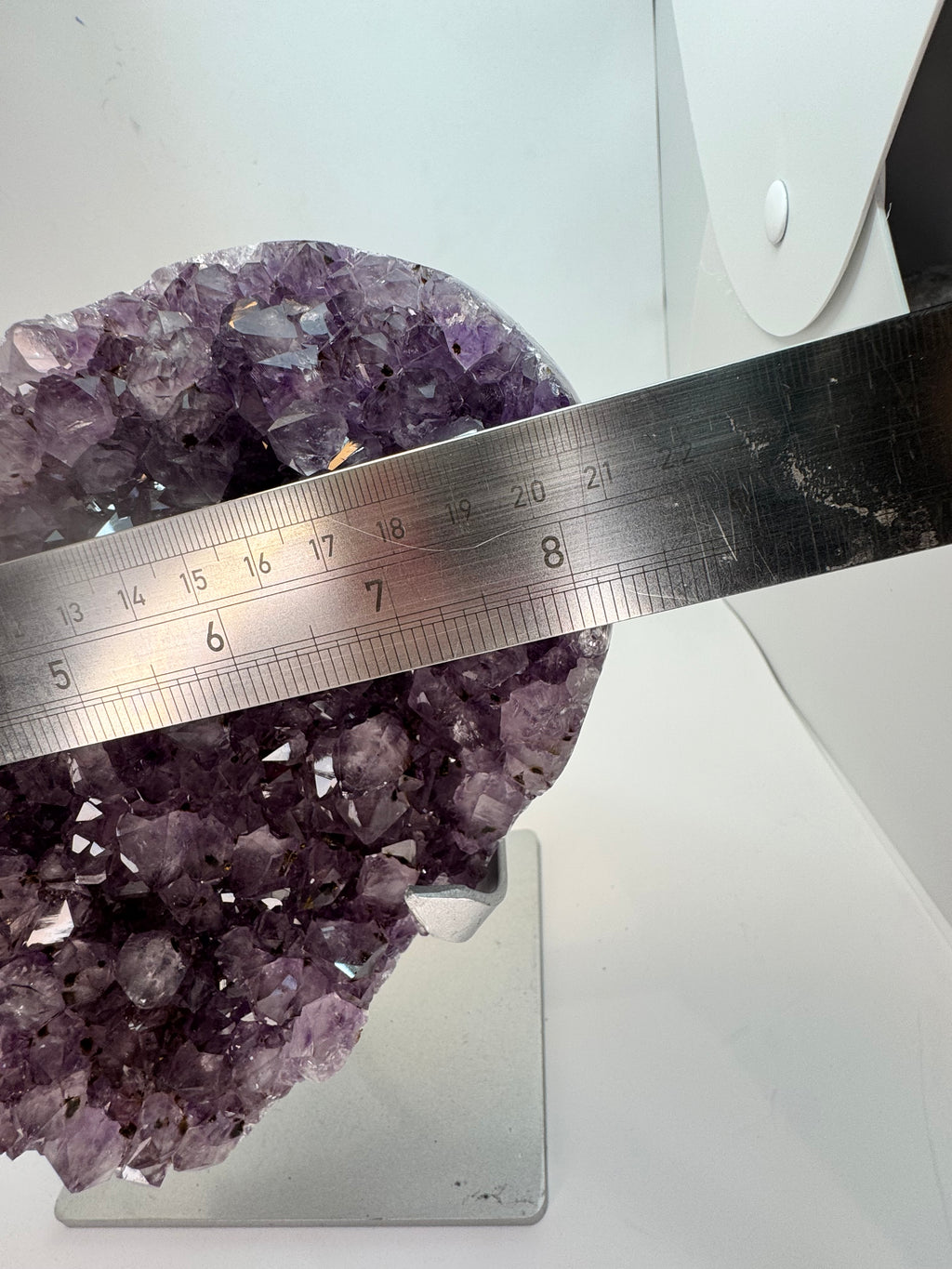 Amethyst crystal cluster with a ruler for scale on a white background